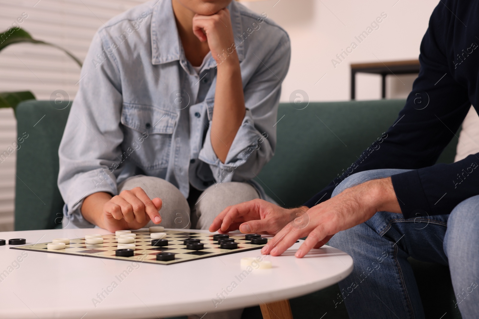 Photo of Couple playing checkers at white table indoors, closeup