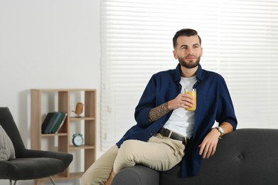 Photo of Handsome man with delicious smoothie on sofa at home. Space for text