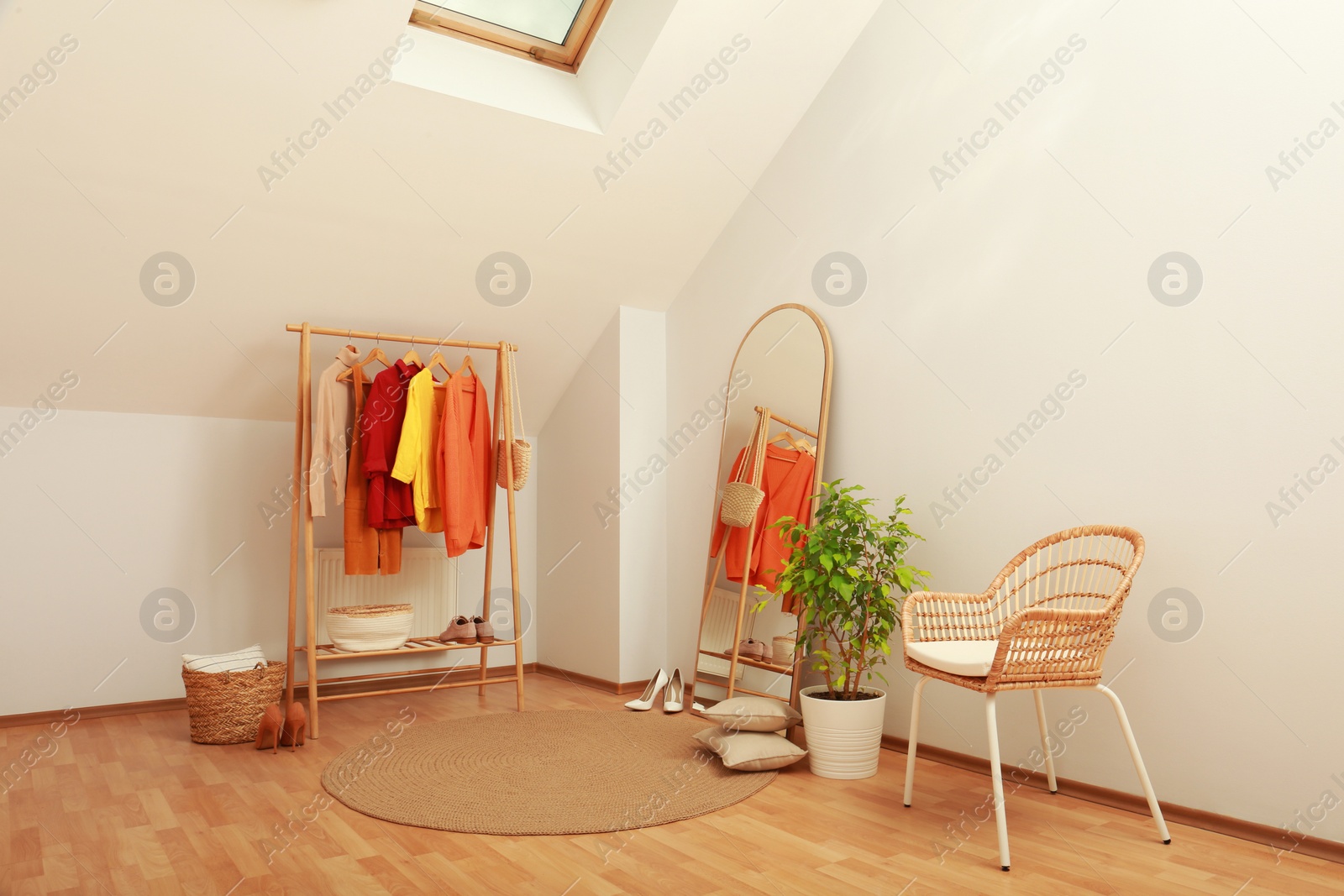 Photo of Stylish clothes rack, mirror and wicker chair in attic room. Interior design