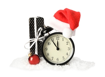 Photo of Alarm clock with Santa hat, gift and Christmas ball in pile of snow on white background. New Year countdown