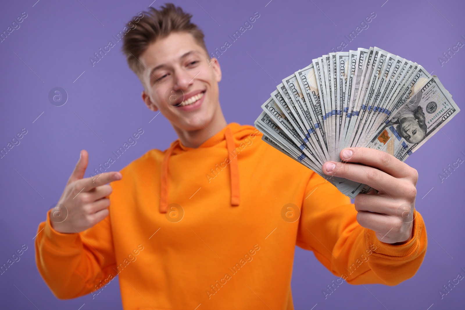 Photo of Happy man pointing at money on purple background, selective focus