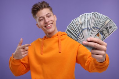 Photo of Happy man pointing at money on purple background, selective focus