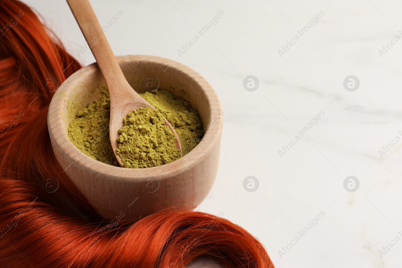 Photo of Bowl of henna powder and red strand on white marble table, closeup with space for text. Natural hair coloring