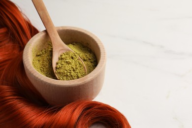 Photo of Bowl of henna powder and red strand on white marble table, closeup with space for text. Natural hair coloring