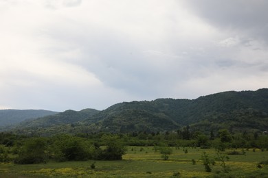 Photo of Picturesque view of mountains, trees and field on cloudy day