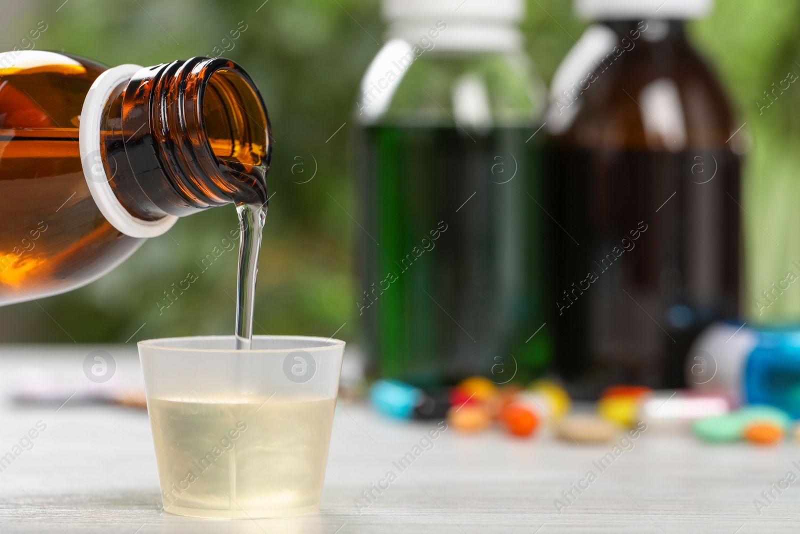Photo of Pouring syrup from bottle into measuring cup on table, closeup with space for text. Cold medicine