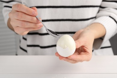 Photo of Woman eating boiled egg with spoon at white wooden table, closeup