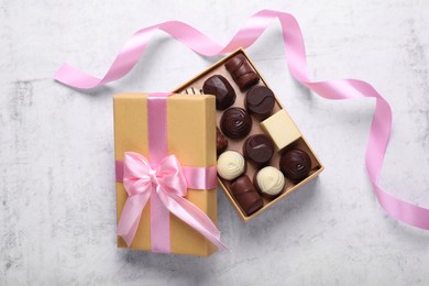 Photo of Open box with delicious chocolate candies and pink ribbon on white table, top view