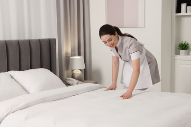 Young chambermaid making bed in hotel room