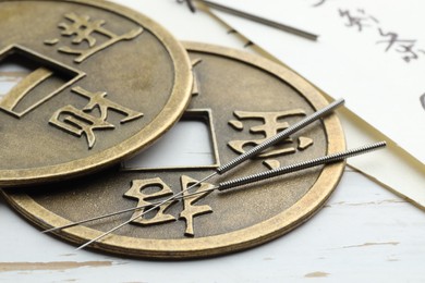 Photo of Acupuncture needles, Chinese coins and sheets of paper with characters on white wooden table, closeup