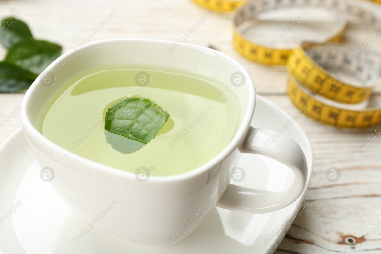 Photo of Cup of diet herbal tea with green leaf on white wooden table, closeup