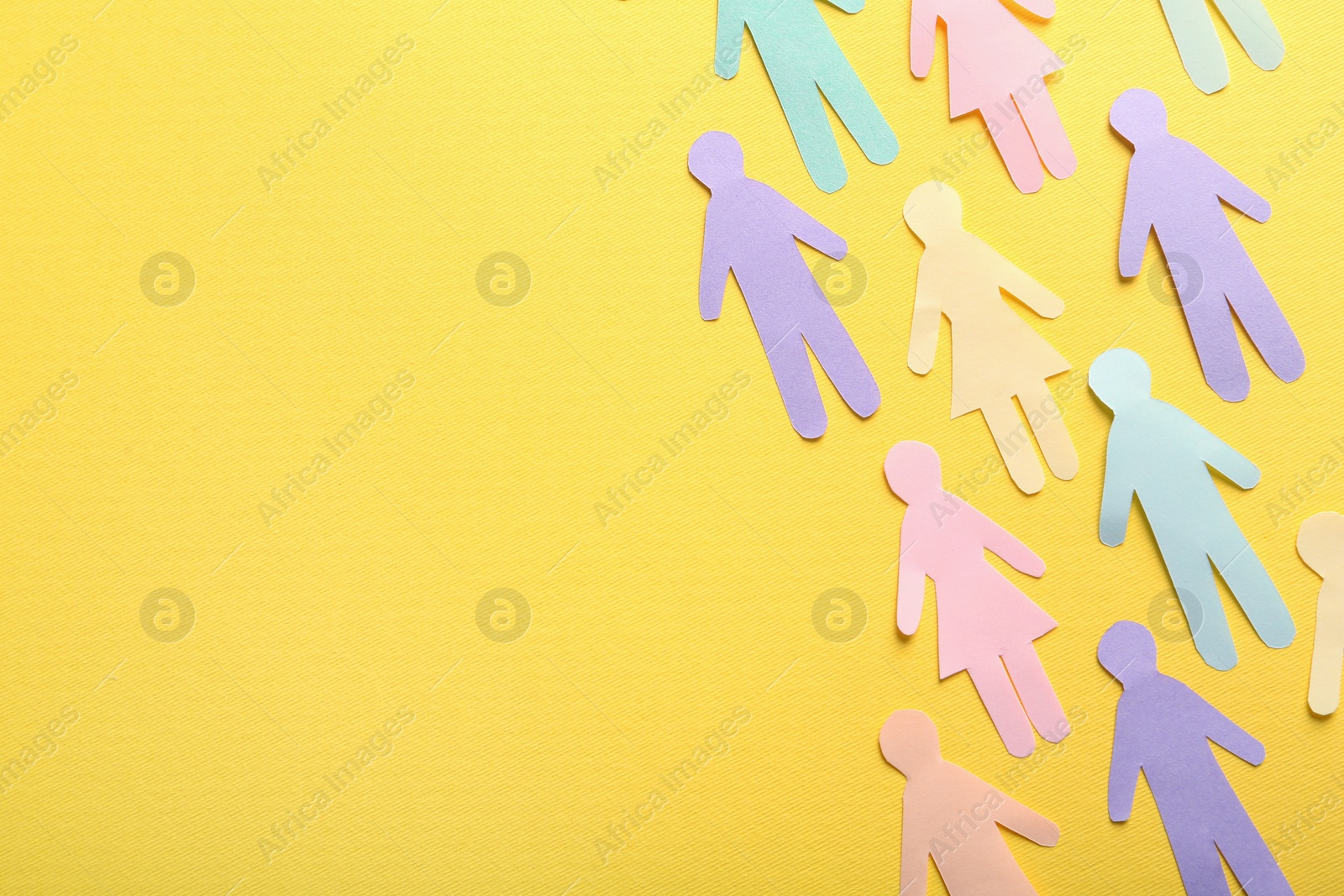 Photo of Many different paper human figures on yellow background, flat lay with space for text. Diversity and inclusion concept