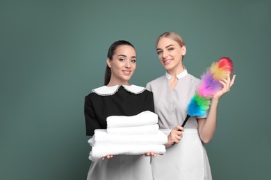 Photo of Young chambermaids with stack of clean towels and dusting brush on color background