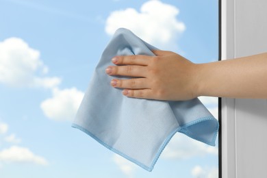 Photo of Woman cleaning window glass with rag indoors, closeup