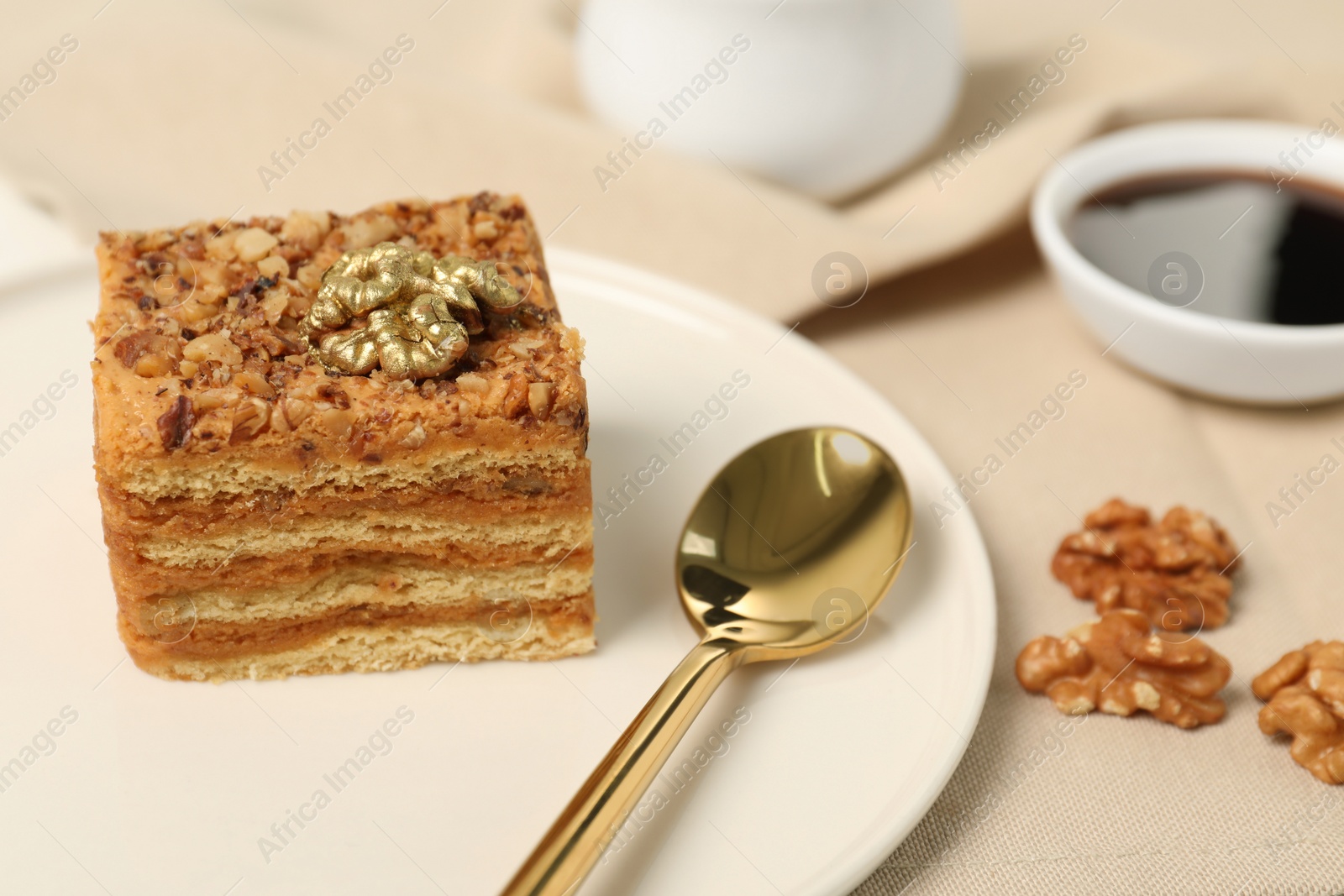 Photo of Piece of delicious layered honey cake, spoon and walnuts on table, closeup. Space for text