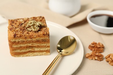 Piece of delicious layered honey cake, spoon and walnuts on table, closeup. Space for text