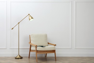 Stylish room interior with lamp and armchair near white wall. Space for text