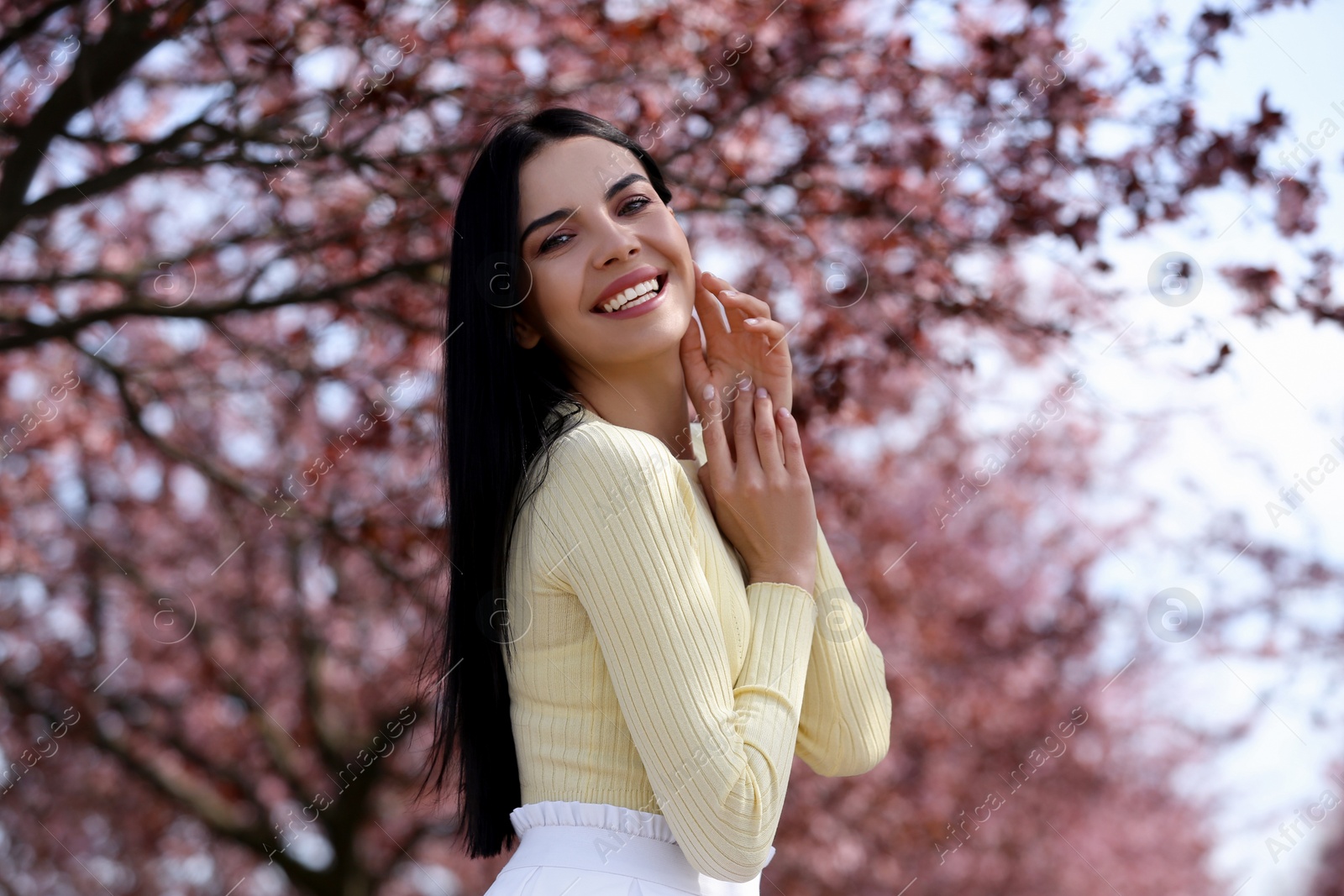 Photo of Pretty young woman near beautiful blossoming trees outdoors. Stylish spring look