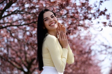 Photo of Pretty young woman near beautiful blossoming trees outdoors. Stylish spring look
