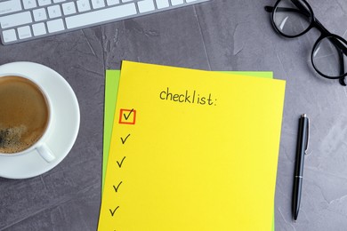 Photo of Paper sheet with inscription Checklist near eyeglasses, computer keyboard and cup of coffee on grey table, flat lay