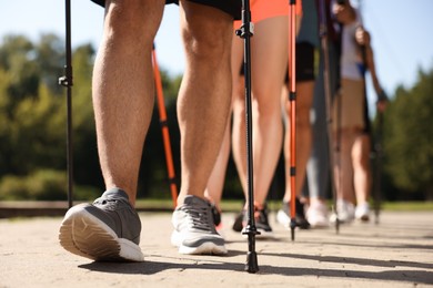 Group of people practicing Nordic walking with poles outdoors on sunny day, closeup