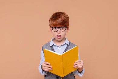 Surprised schoolboy with book on beige background