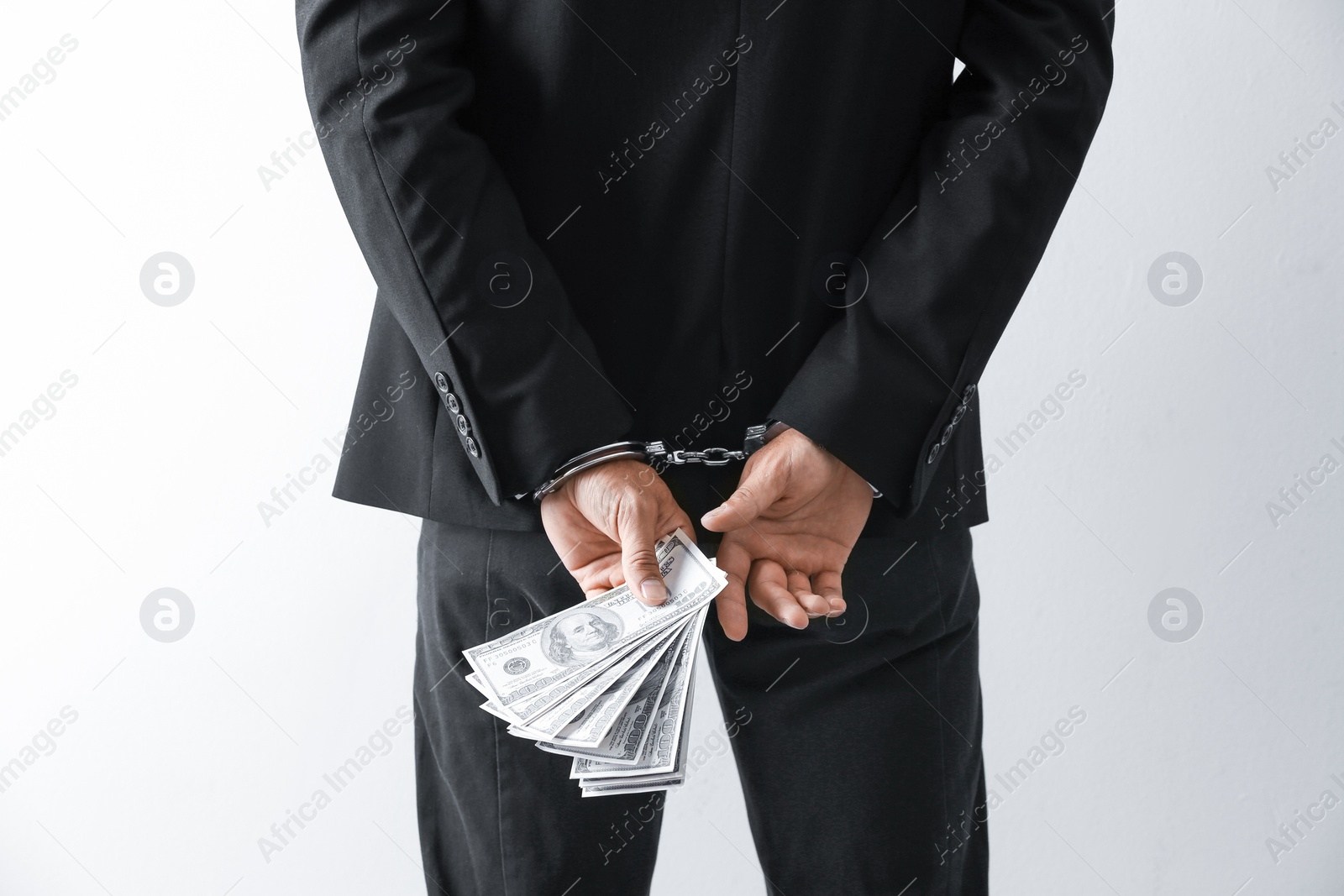 Photo of Man in handcuffs holding bribe money on light background, closeup