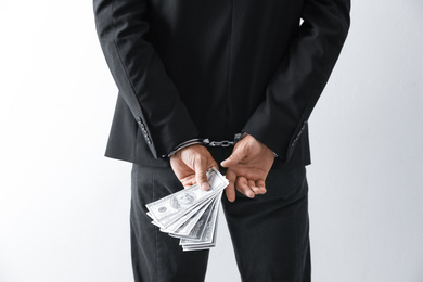 Photo of Man in handcuffs holding bribe money on light background, closeup
