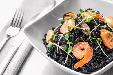 Delicious black risotto with seafood in bowl on table, closeup