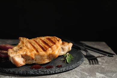 Photo of Grilled meat served with rosemary and sauce on slate plate against black background. Space for text