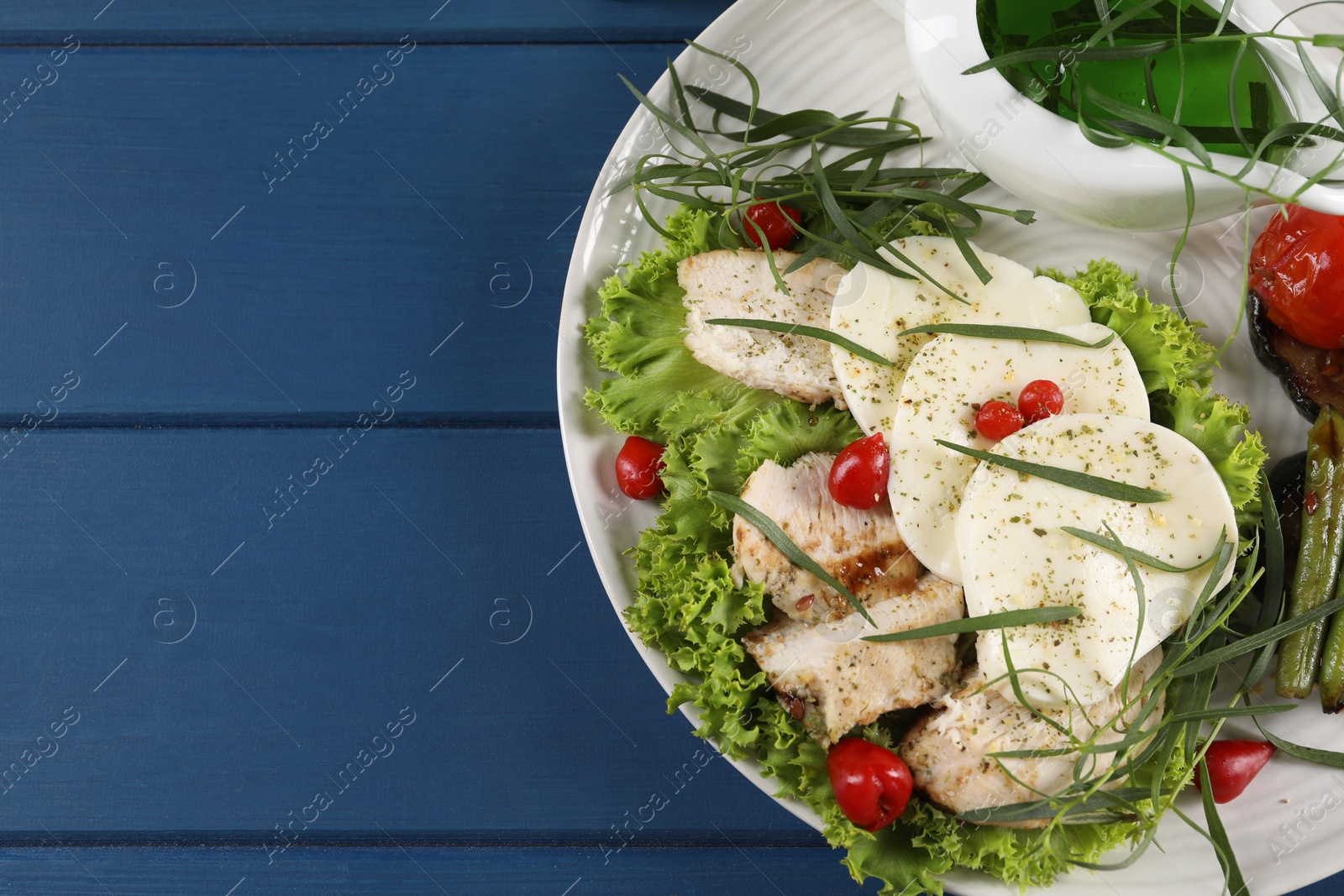 Photo of Tasty mozzarella, chicken and vegetables with tarragon on blue wooden table, top view. Space for text