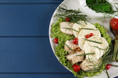 Tasty mozzarella, chicken and vegetables with tarragon on blue wooden table, top view. Space for text