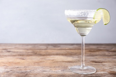 Photo of Glass of lemon drop martini cocktail with lime slice on wooden table against light background. Space for text