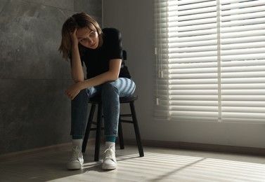 Sad young woman sitting on chair at home, space for text