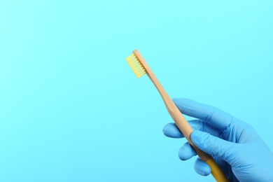 Photo of Dentist holding wooden toothbrush on color background, space for text