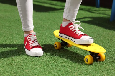 Photo of Woman with penny board wearing red classic old school sneakers on green grass outdoors, closeup