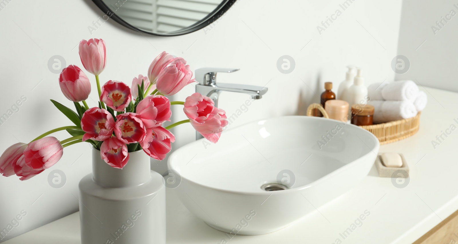 Photo of Vase with beautiful pink tulips and toiletries near sink in bathroom