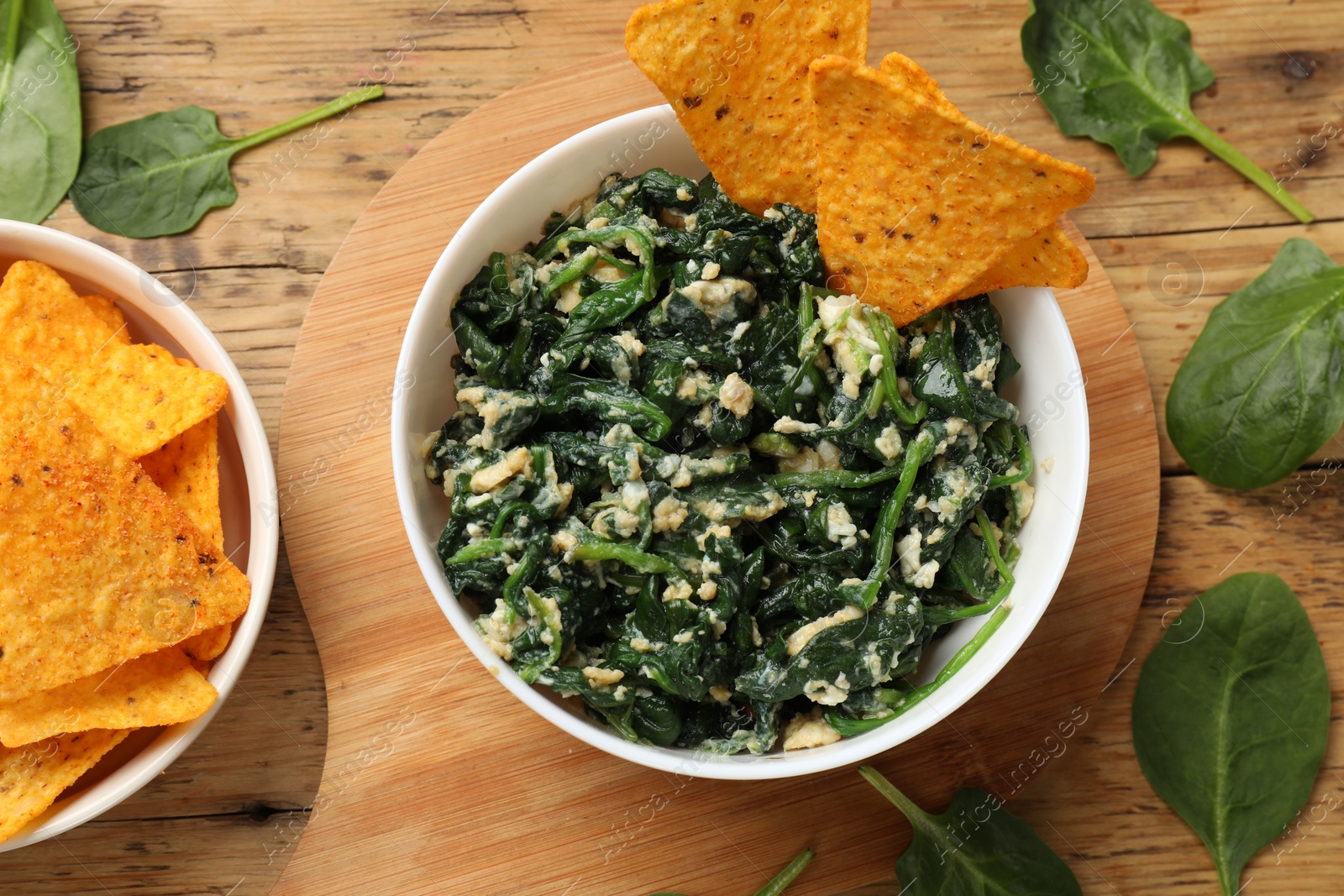 Photo of Tasty spinach dip with eggs in bowl and nachos chips on wooden table, flat lay