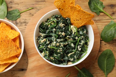 Photo of Tasty spinach dip with eggs in bowl and nachos chips on wooden table, flat lay