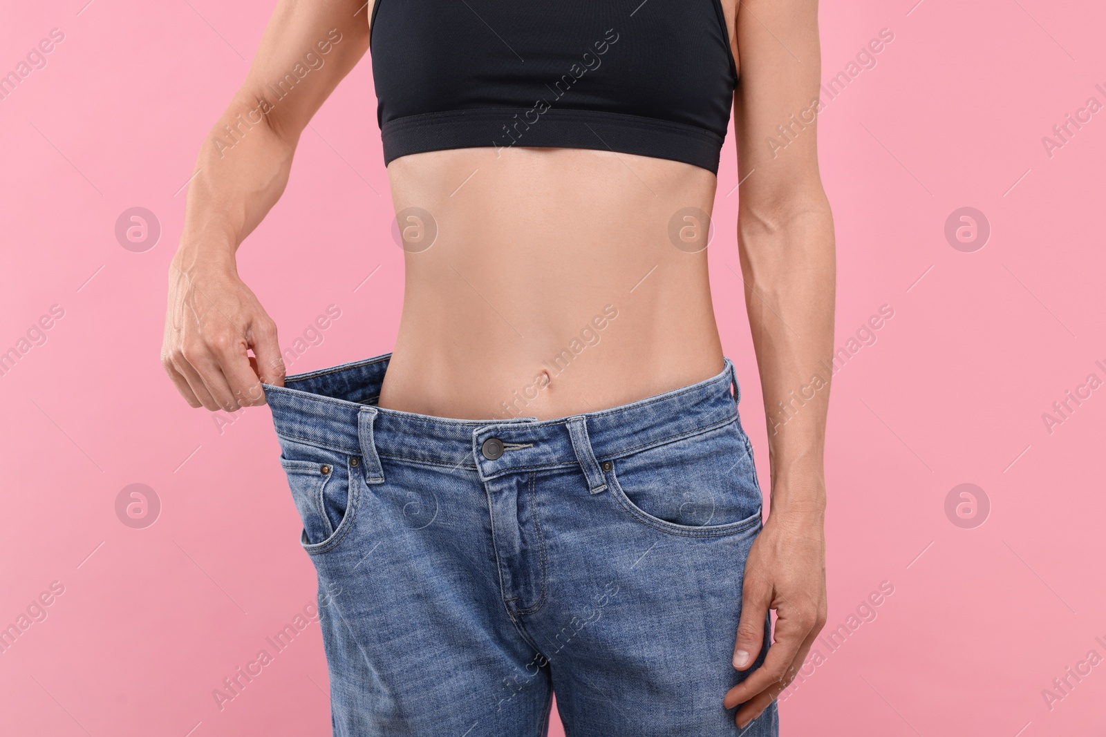 Photo of Slim woman wearing big jeans on pink background, closeup. Weight loss