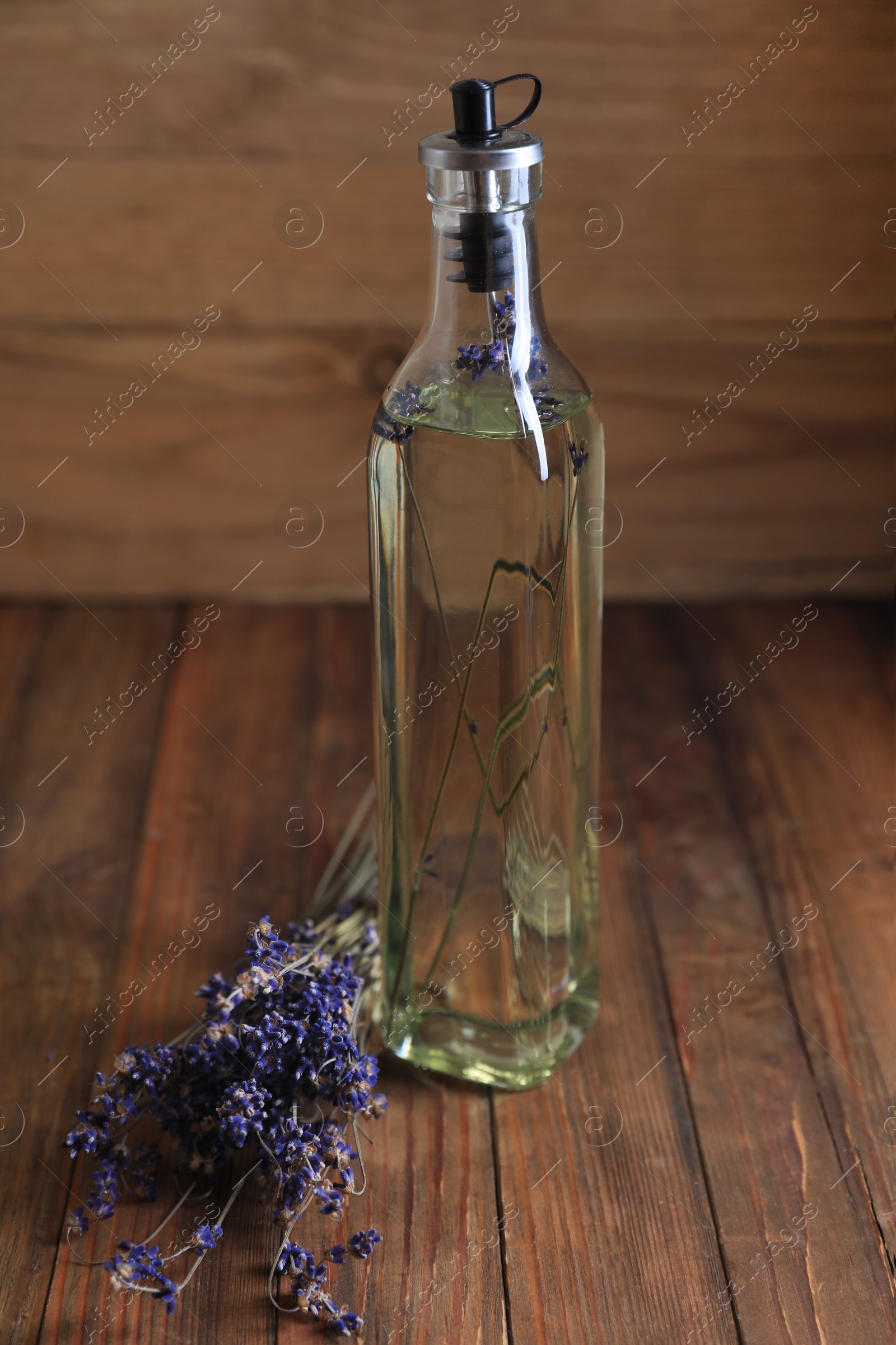 Photo of Bottle of cooking oil and lavender flowers on wooden table