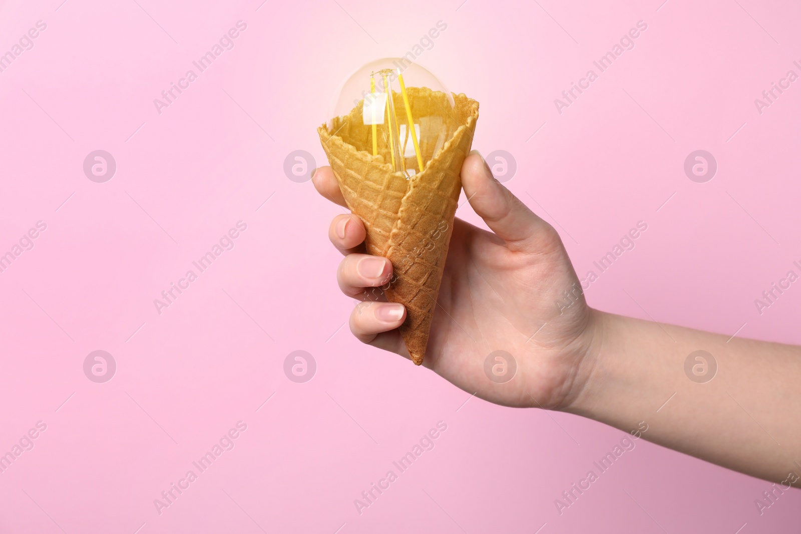 Photo of Woman holding waffle ice cream cone with light bulb on pink background, closeup