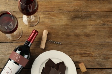 Flat lay composition with tasty red wine and chocolate on wooden table. Space for text