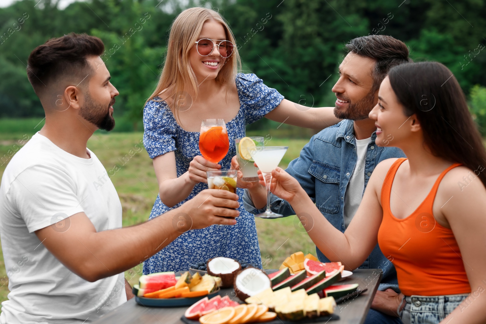 Photo of Happy friends clinking glasses of cocktails at table outdoors