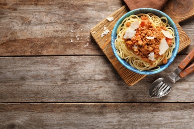 Photo of Bowl with delicious pasta bolognese on wooden table, top view