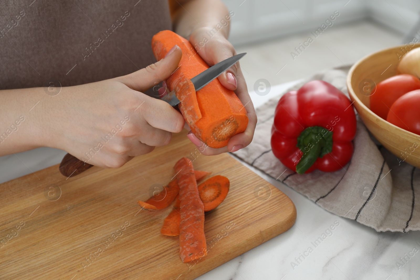 Photo of Woman peeling fresh carrot with knife at white marble table, closeup