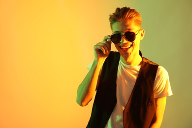 Photo of Stylish young man in sunglasses on color background in neon lights. Space for text