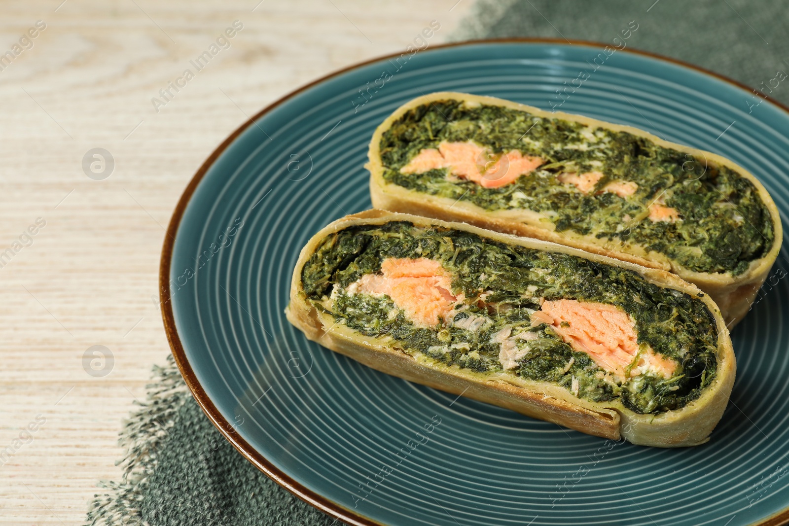 Photo of Pieces of delicious strudel with salmon and spinach on white wooden table, closeup