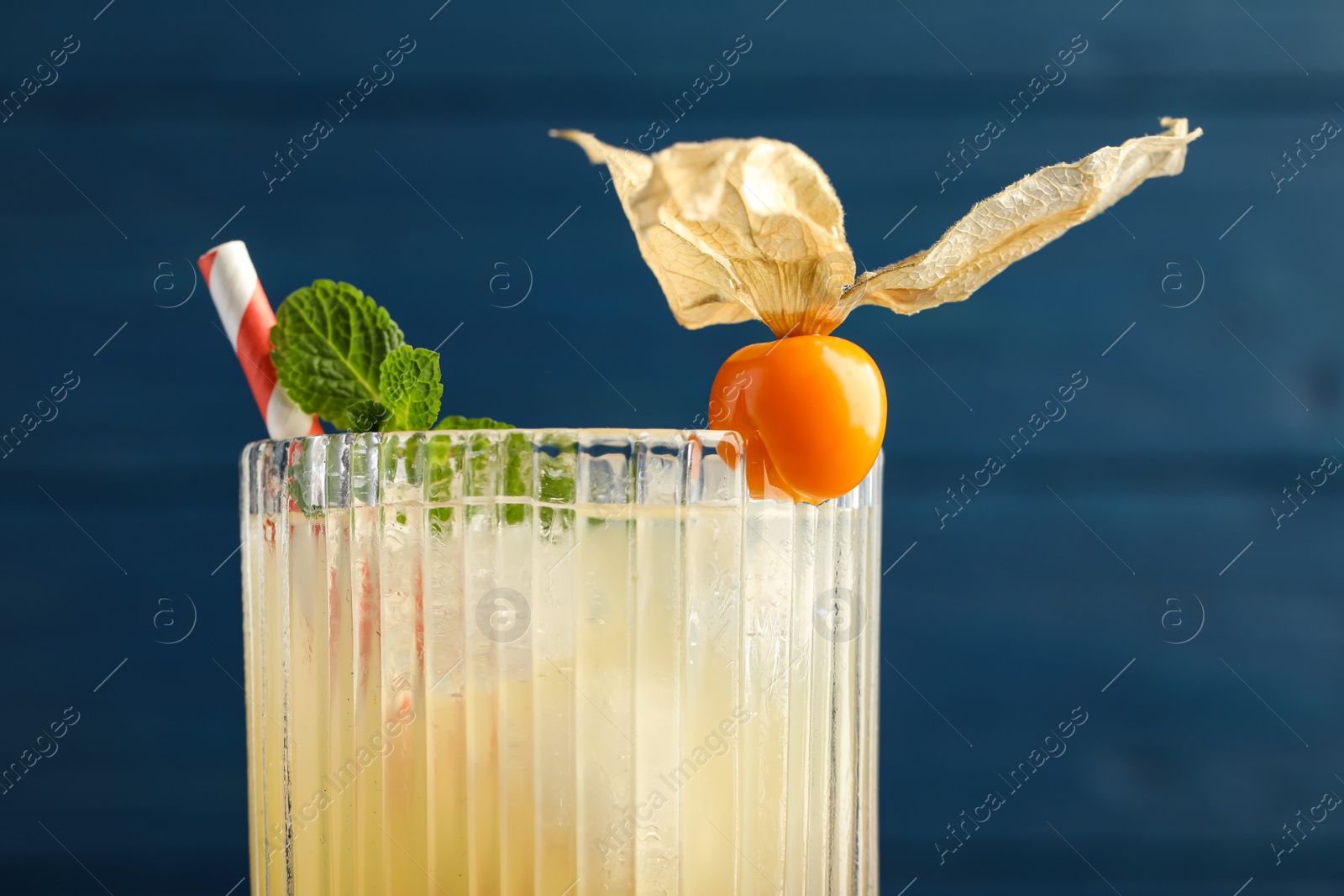 Photo of Refreshing cocktail decorated with physalis fruit on blue background, closeup