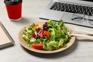 Photo of Fresh vegetable salad, laptop and paper cup of coffee on white wooden table at workplace. Business lunch